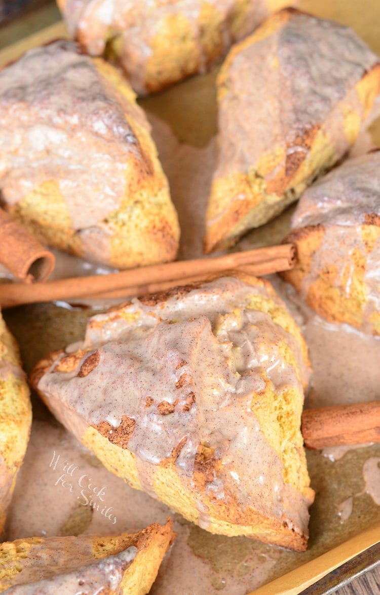 Glazed Cinnamon Swirled Scones on parchment paper with cinnamon sticks around it 