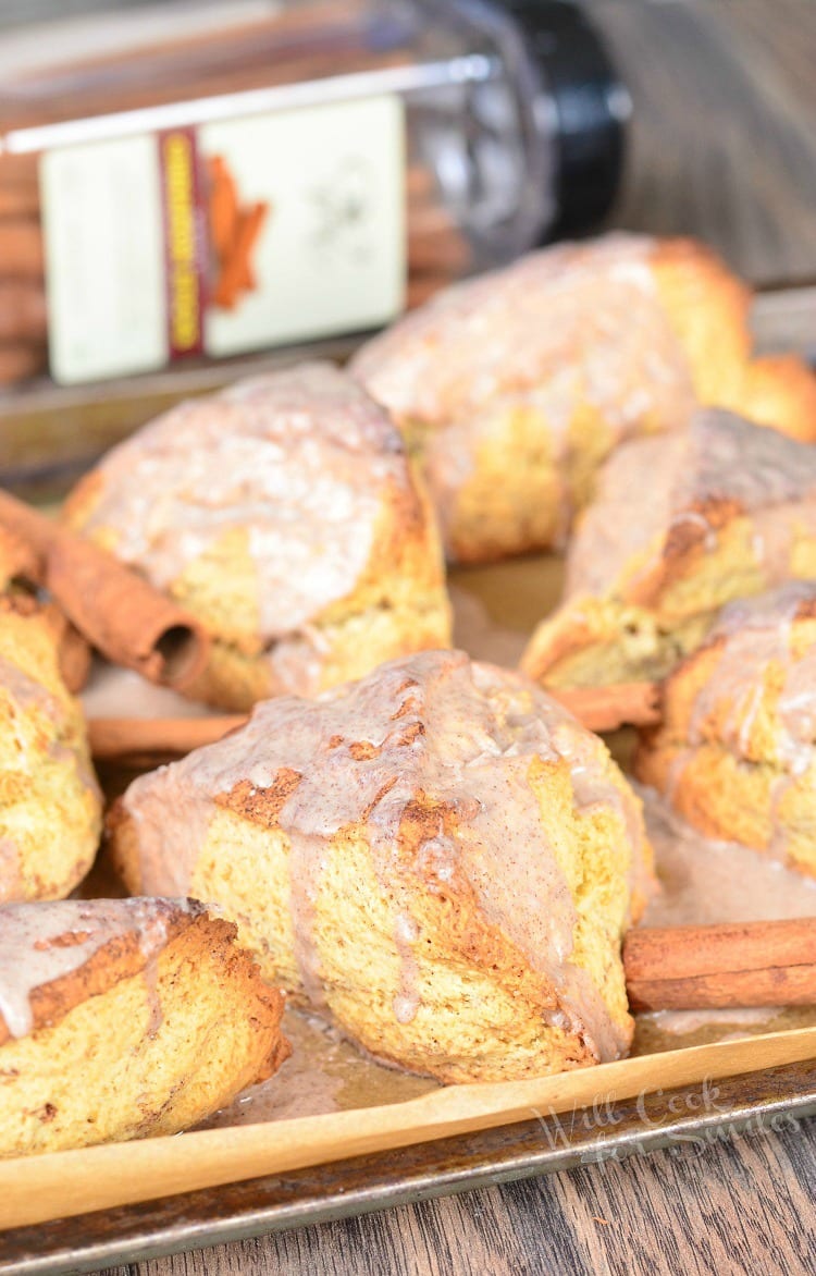 Glazed Cinnamon Swirled Scones on parchment paper with cinnamon sticks around it 