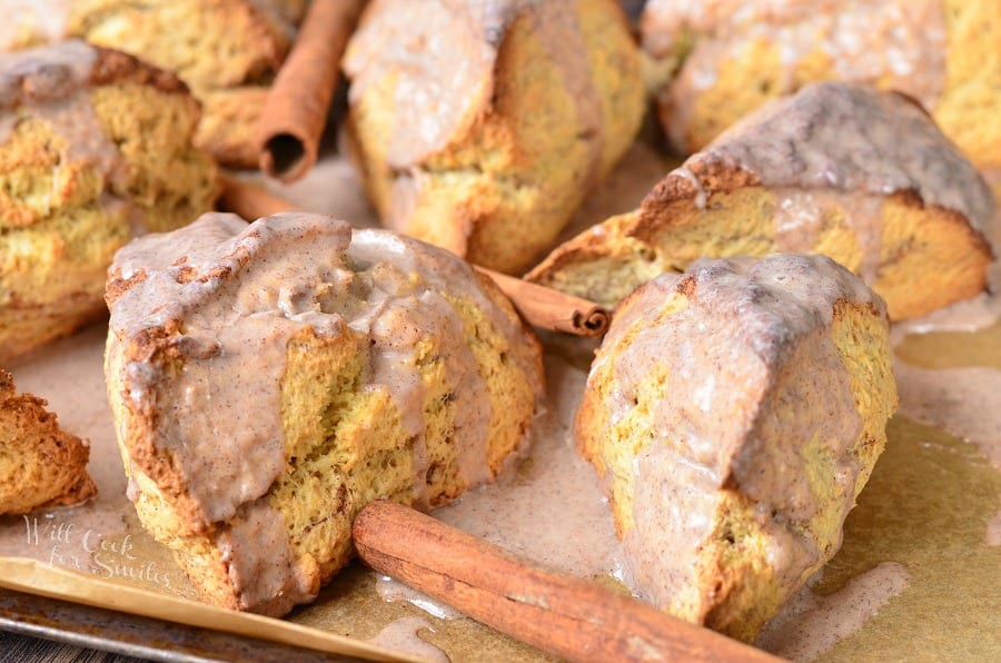 horizonal photo Glazed Cinnamon Swirled Scones on parchment paper with cinnamon sticks around it 