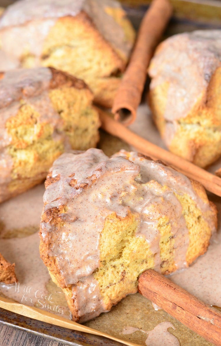 Glazed Cinnamon Swirled Scones on a baking sheet with cinnamon sticks around it 