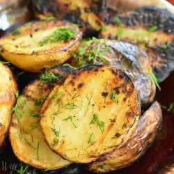 Herbed grilled potatoes on a brown and white platter on a wooden table topped with dill