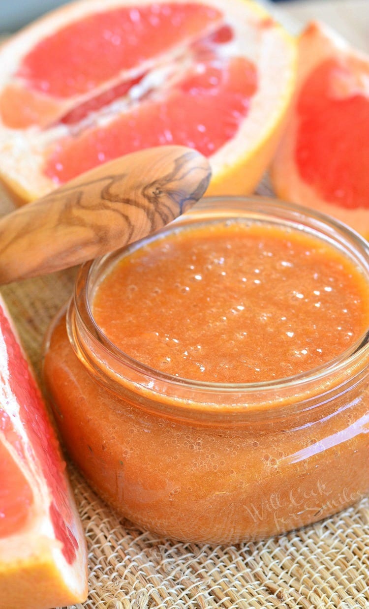 Homemade Grapefruit Sauce  in a glass jar with a wood lid leaning on it and cut up grapefruit in the back ground 