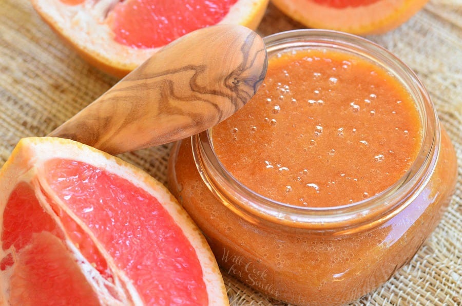 Homemade Grapefruit Sauce with wood lid leaning on it and cut up grapefruit around it 