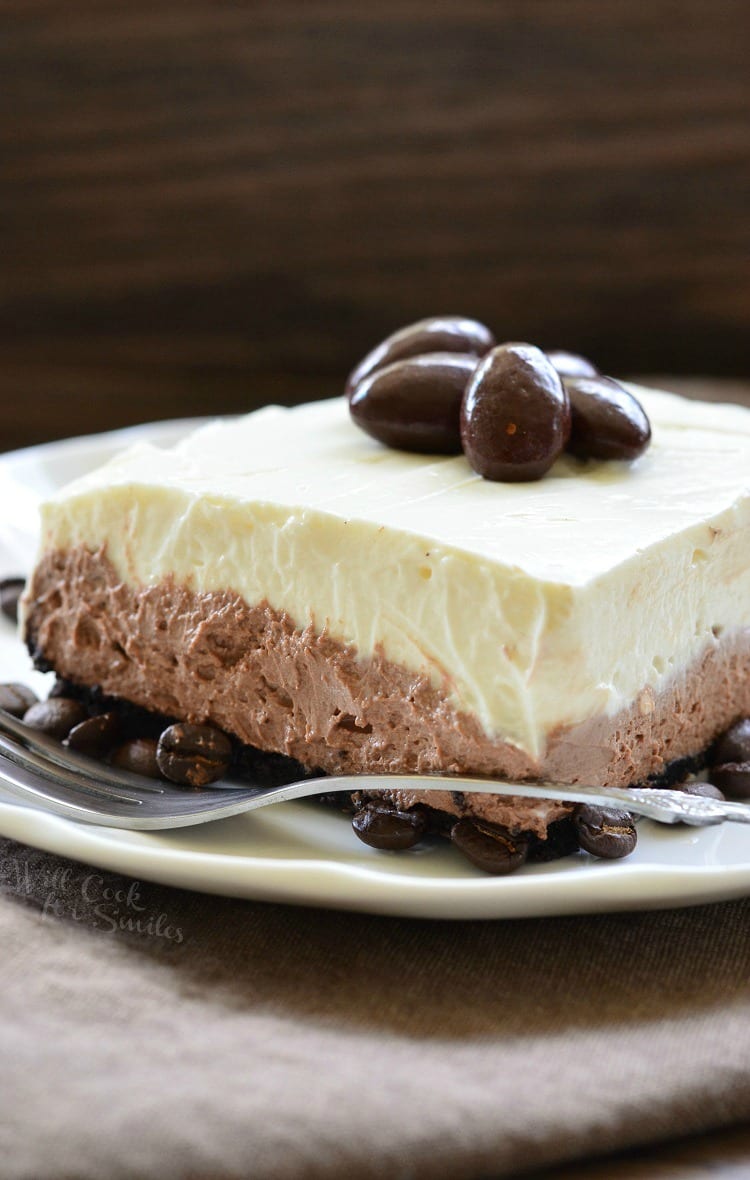 Layered Chocolate Espresso Cheesecake Dessert with chocolate covered espresso beans on top on a white plate with a fork over the front of the plate 