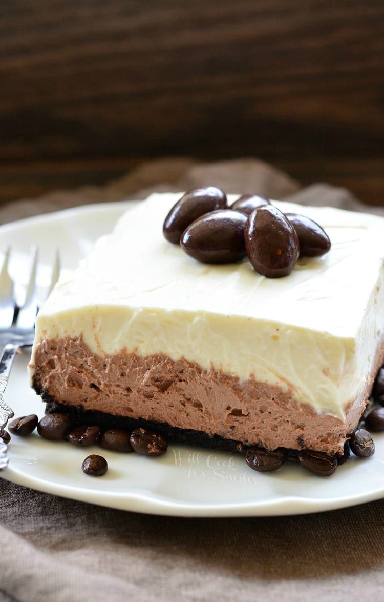 Layered Chocolate Espresso Cheesecake Dessert with chocolate covered espresso beans on top on a white plate with a fork to the left 