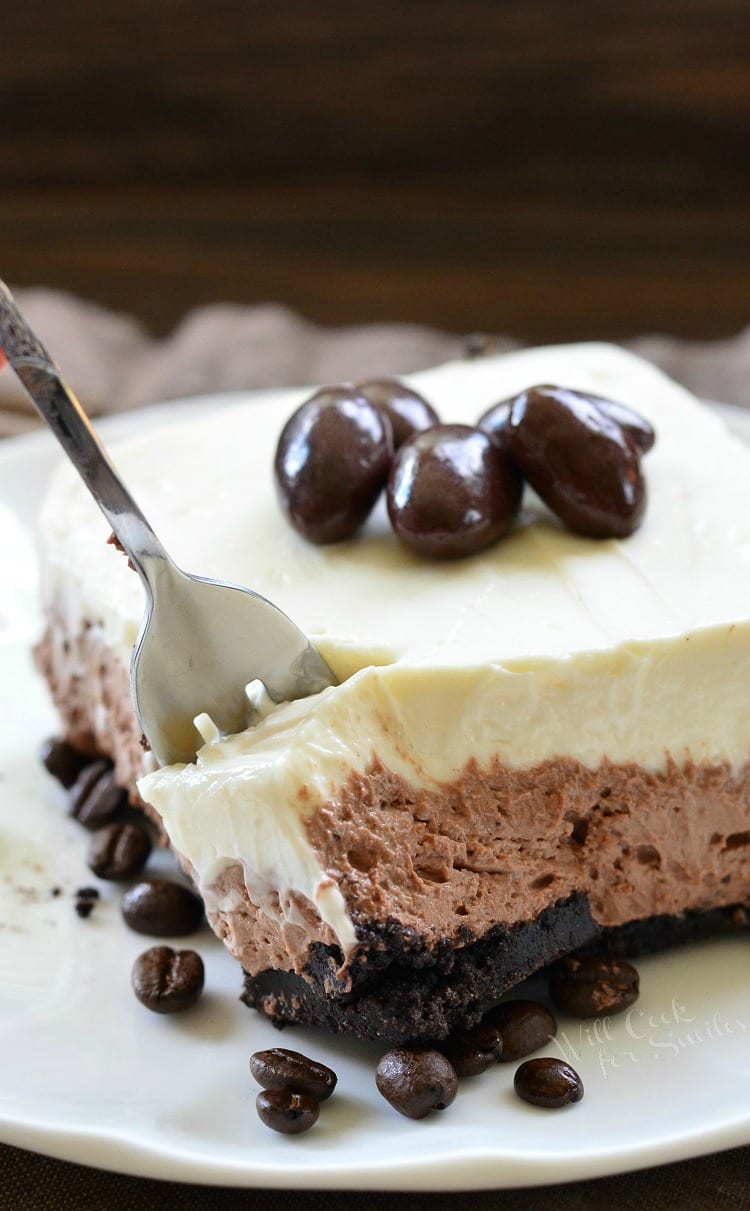 Layered Chocolate Espresso Cheesecake Dessert with chocolate covered espresso beans on top on a white plate with a fork being put in it 