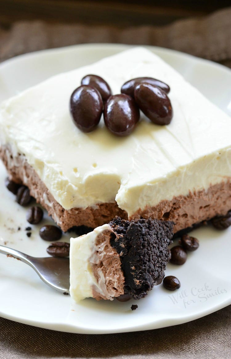 Layered Chocolate Espresso Cheesecake Dessert with chocolate covered espresso beans on top on a white plate with a fork to the left with a some of the cake on it 