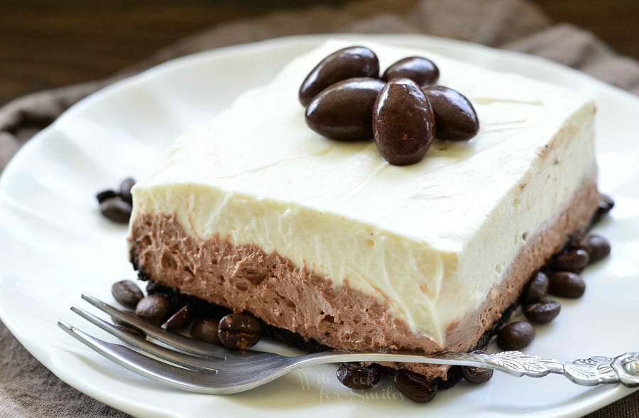 Layered Chocolate Espresso Cheesecake Dessert with chocolate covered espresso beans on top on a white plate with a fork over the front of the plate 