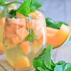 2 glasses filled with melon mint wine spritzer topped with mint leaves on a wooden table as viewed close up