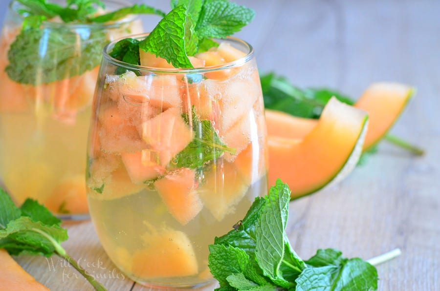 horizonal photo of Melon Mint Wine Spritzer with cantaloupe and mint in a stemless wine glass with mint on top as a garnish and cantaloupe slices in the background 