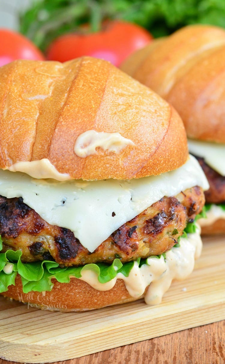 Chicken Burger with cheese on a bun with lettuce and sauce on a wood cutting table 