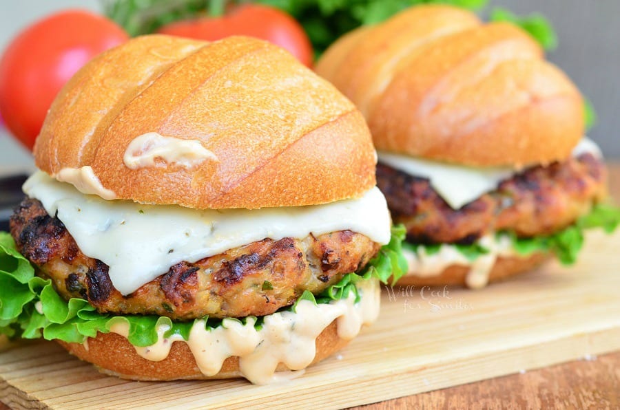 Chicken Burger with cheese on a bun with lettuce and sauce on a wood cutting table 