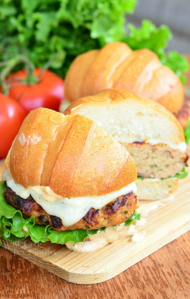 Chicken Burger with cheese on a bun with lettuce and sauce cut in half on a wood cutting table 