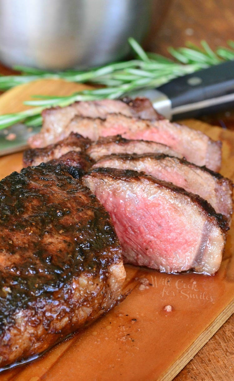 sliced steak on the cutting board with rosemary and a knife on the background