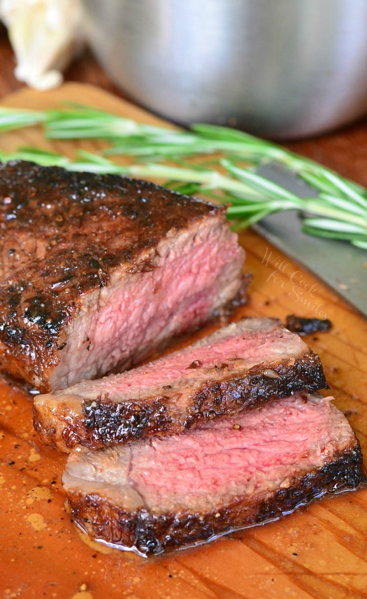 Steak sliced on a cutting board with rosemary in the background 