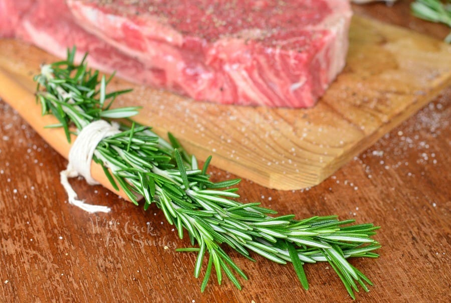 rosemary tied to the end of the brush and raw steak on the background