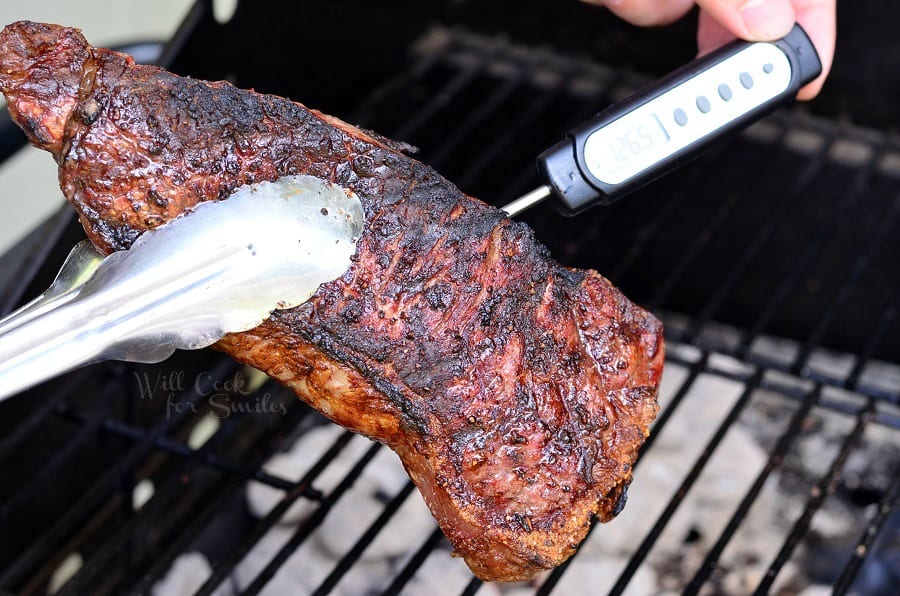 taking temperature of the steak while holding it with a metal tongues 