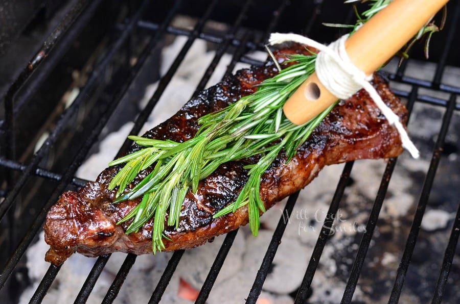 brushing cooked steak with a rosemary brush and butter