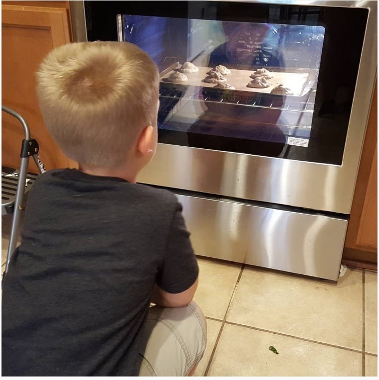 my little man sitting in front of the oven watching the cookies inside bake 