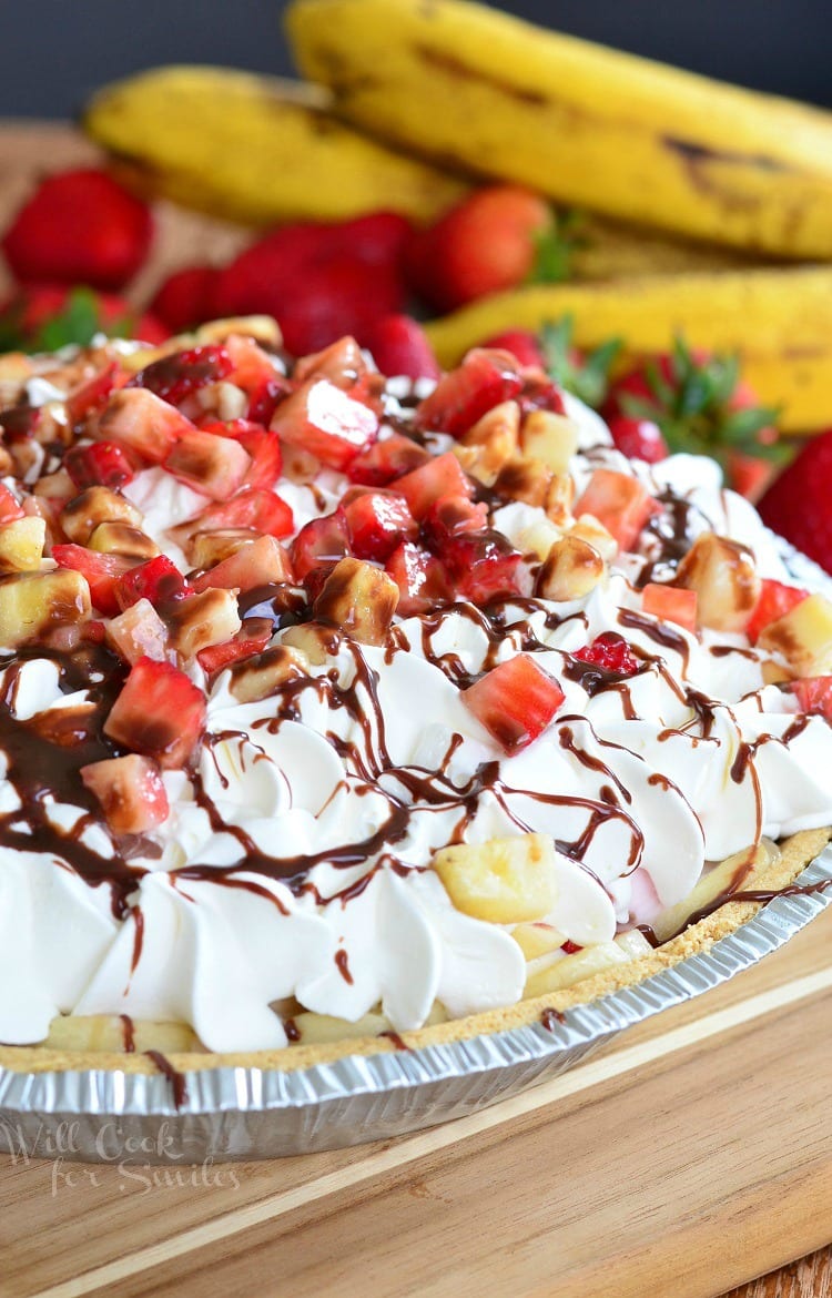 Banana Split Ice Cream Pie in a disposable metal pie pan with whipped cream, strawberries, banana, and chocolate syrup on top on a table 