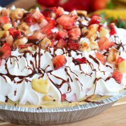 Banana Split Ice Cream Pie on a wooden table with bananas and strawberries in the background as viewed close up