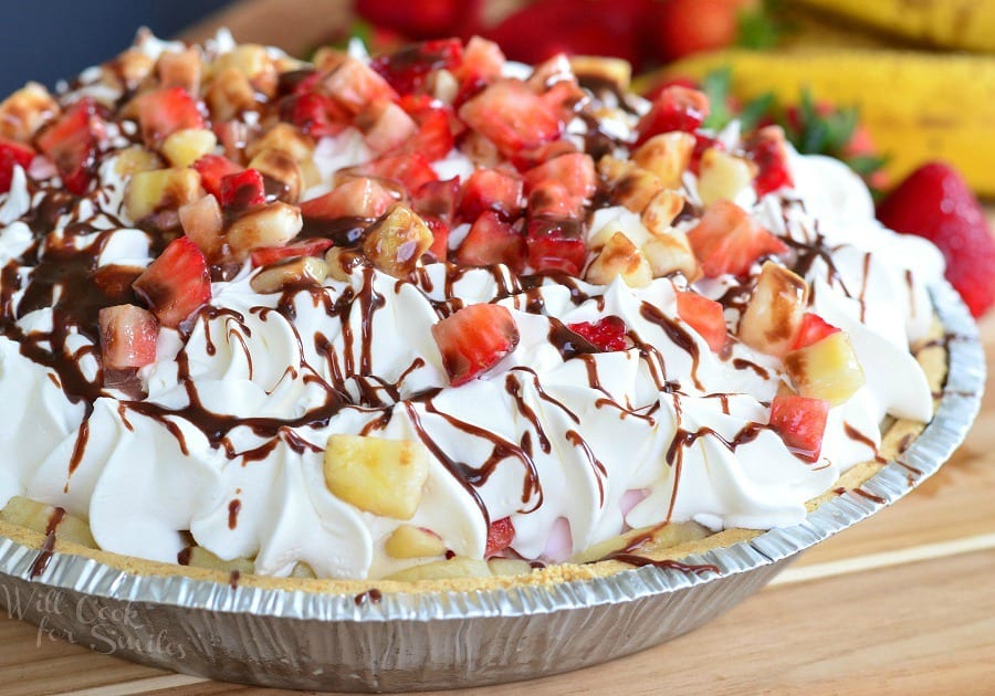 Banana Split Ice Cream Pie in a disposable metal pie pan with whipped cream, strawberries, banana, and chocolate syrup on top on a table 