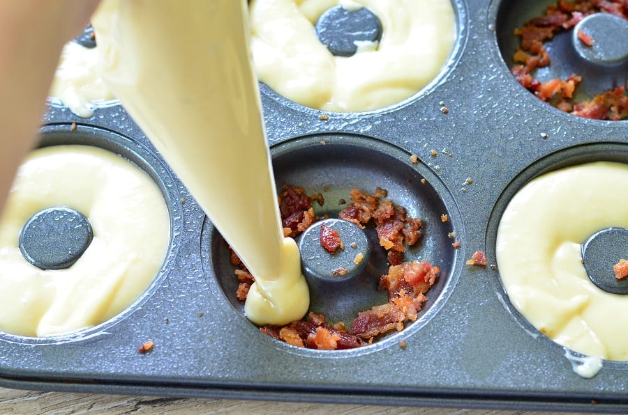 pipping donut batter into donut pan that has bacon in it 