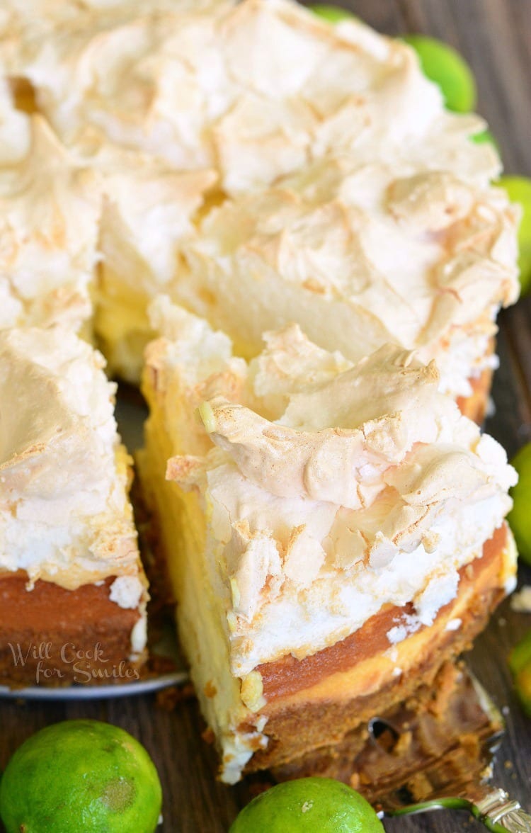 top view photo of Key Lime Pie Cheesecake with meringue on top with a slice being lifted out with a pie spatula on a table with limes 