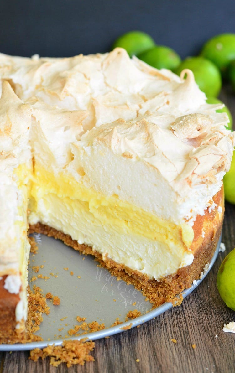 1 slice missing from a whole cheesecake with limes in the background