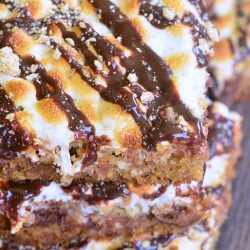 3 layered double chocolate S'Mores crumble cookie bars stacked on top of each other on a dark wooden table as viewed from above