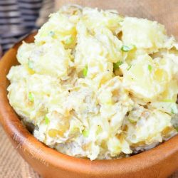 Wooden bowl filled with roasted garlic asiago potato salad on a tan cloth as viewed close up