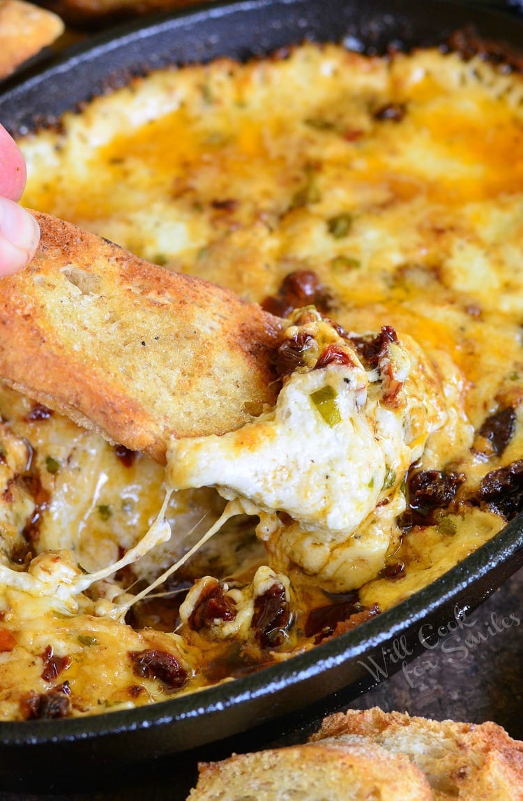 dipping toasted bread into Smokey Sun-Dried Tomato and Basil Mozzarella Dip in a cast iron pan 