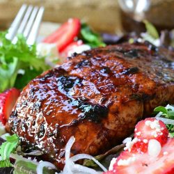 Strawberry balsamic glazed baked salmon salad with a fork to the left and a glass container of balsamic dressing in the background