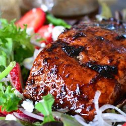 Strawberry balsamic glazed baked salmon salad with a fork to the left and a glass container of balsamic dressing in the background