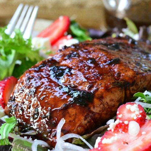 Strawberry balsamic glazed baked salmon salad with a fork to the left and a glass container of balsamic dressing in the background
