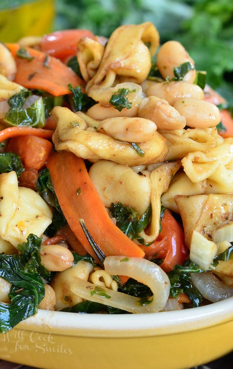 Tortellini pasta with carrots, onions, tomato in a yellow bowl 