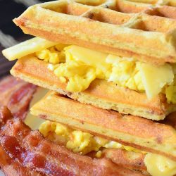 Savory waffles stacked and plated with bacon and onion and a side of eggs in between waffles