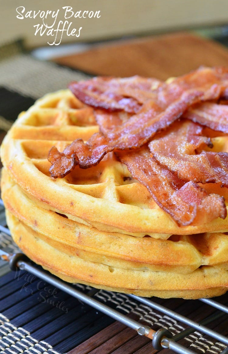 Savory waffles stacked on a metal rack with strips of bacon piled on top of top waffle