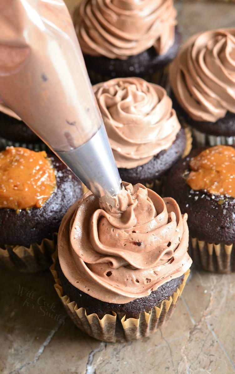 piping chocolate whipped cream frosting on top of chocolate cupcakes filled with Dulce de Leche Filling