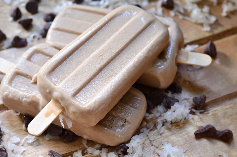 Coconut Mocha Ice Pops stacked up on a cutting board with coconut flakes and chocolate chips 