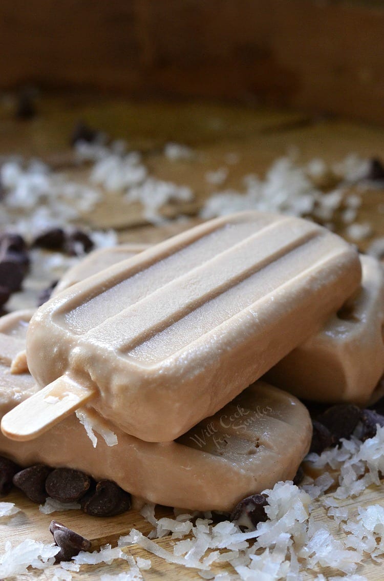 Coconut Mocha Ice Pops stacked up on a cutting board with coconut flakes and chocolate chips 