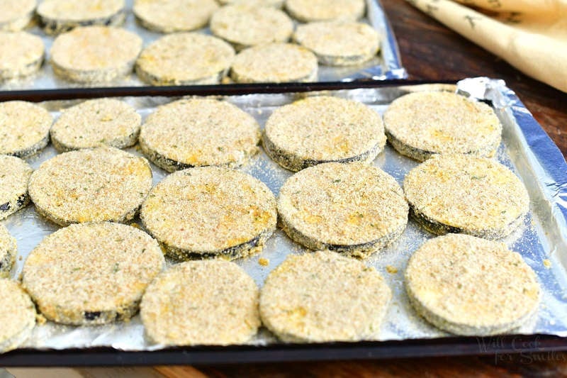 breaded eggplant slices laid out in one layer on two baking sheets
