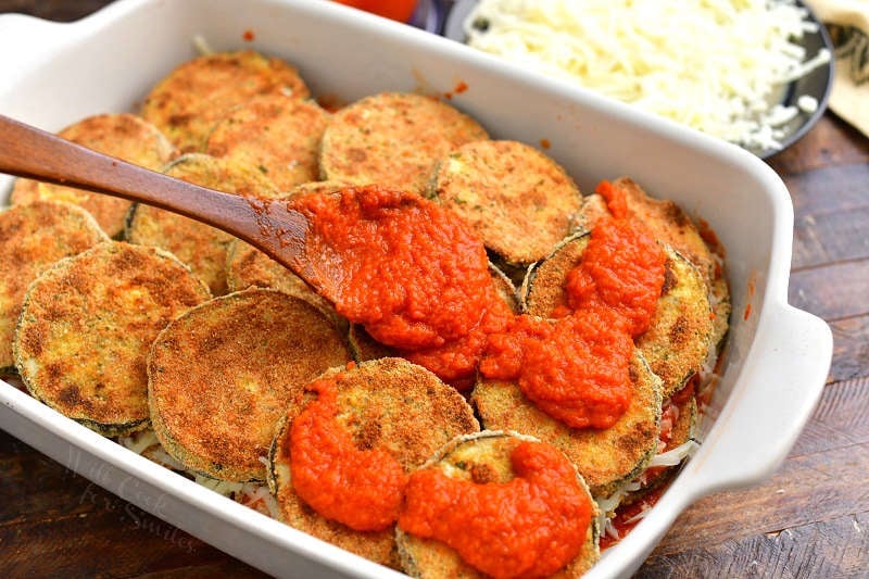 spreading some marinara sauce over the baked crispy eggplant slices with a wooden spoon