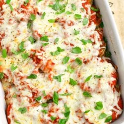 baked eggplant parmesan in a white casserole dish topped with fresh basil leaves and the dish is standing on a burlap towel