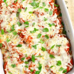 baked eggplant parmesan in a white casserole dish topped with fresh basil leaves and the dish is standing on a burlap towel