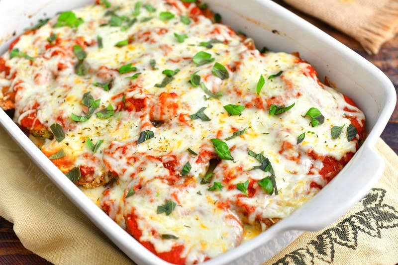 closer view of baked eggplant parmesan in a white casserole dish on to of a burlap towel