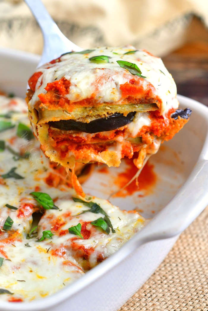 pulling some of the eggplant parmesan out of the baking dish with gooey cheese coming off of the side of the spatula