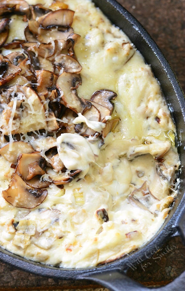 dipping a pretzel into Mushroom Leek and Gruyere Cheese Dip with mushrooms on the top in a cast iron pan 
