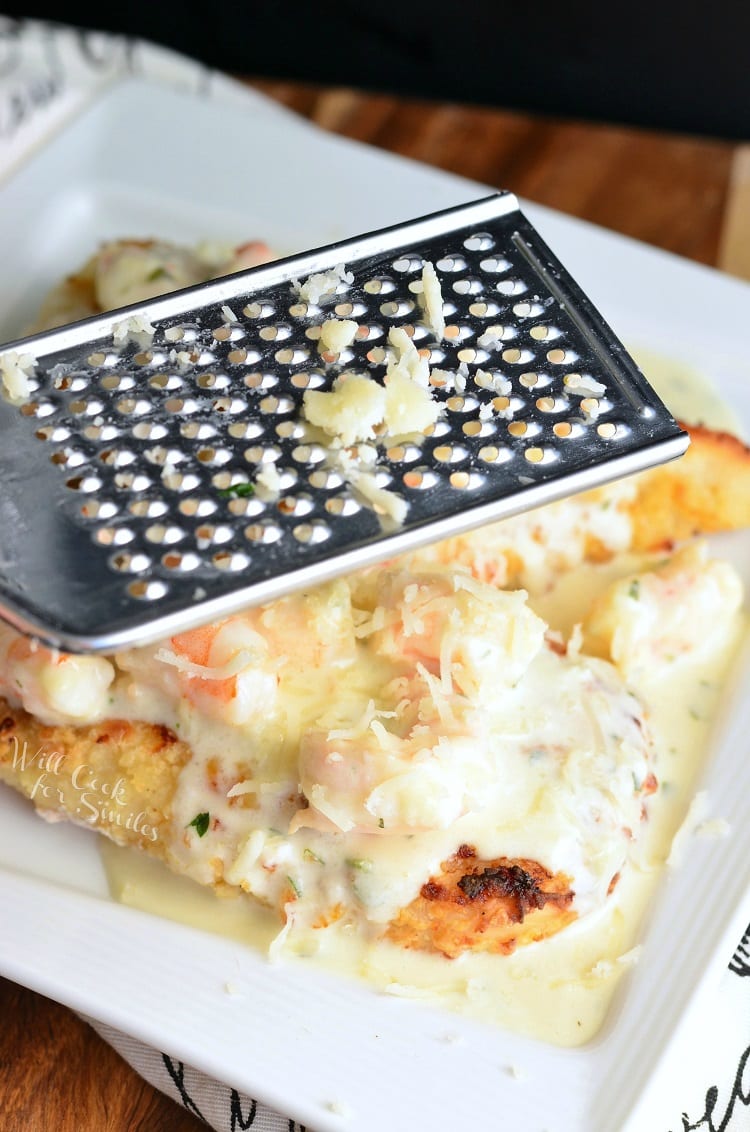 grating cheese with a cheese grater over Oven Fried Chicken topped with shrimp and a Creamy Fontina cheese Shrimp Sauce on a white plate