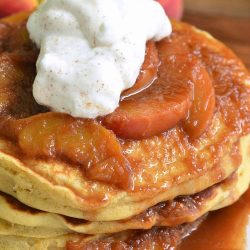 Stack of peaches and cream fluffy buttermilk pancakes on a white decorative plate with peaches in the background